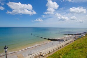 A coastal beach with a promenade, a pier extending into the sea, and a clear sky.