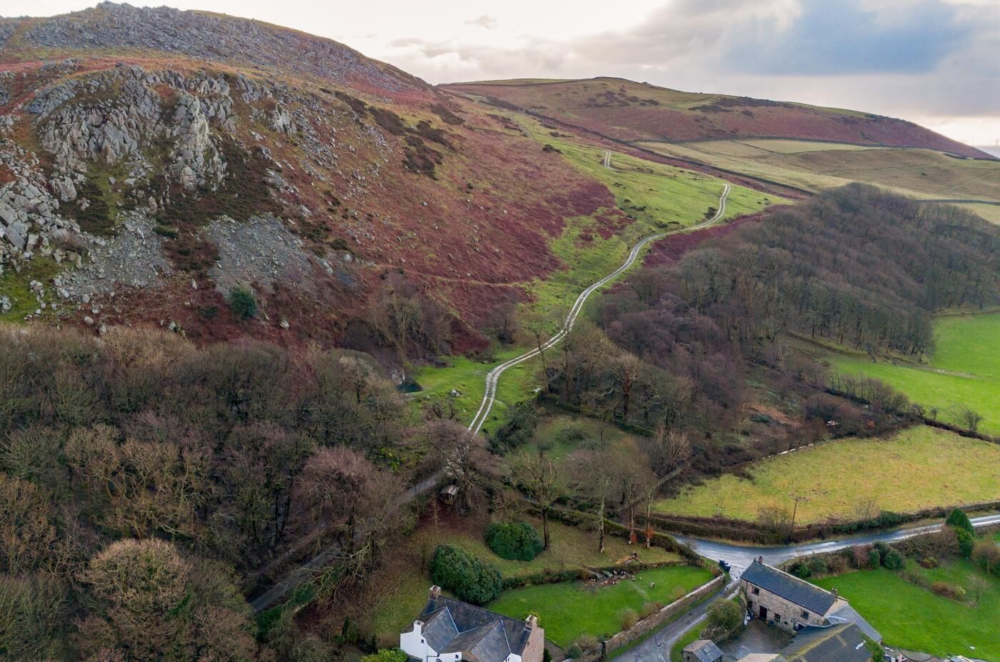 A rural landscape with a winding road, a stone house, and surrounding fields.