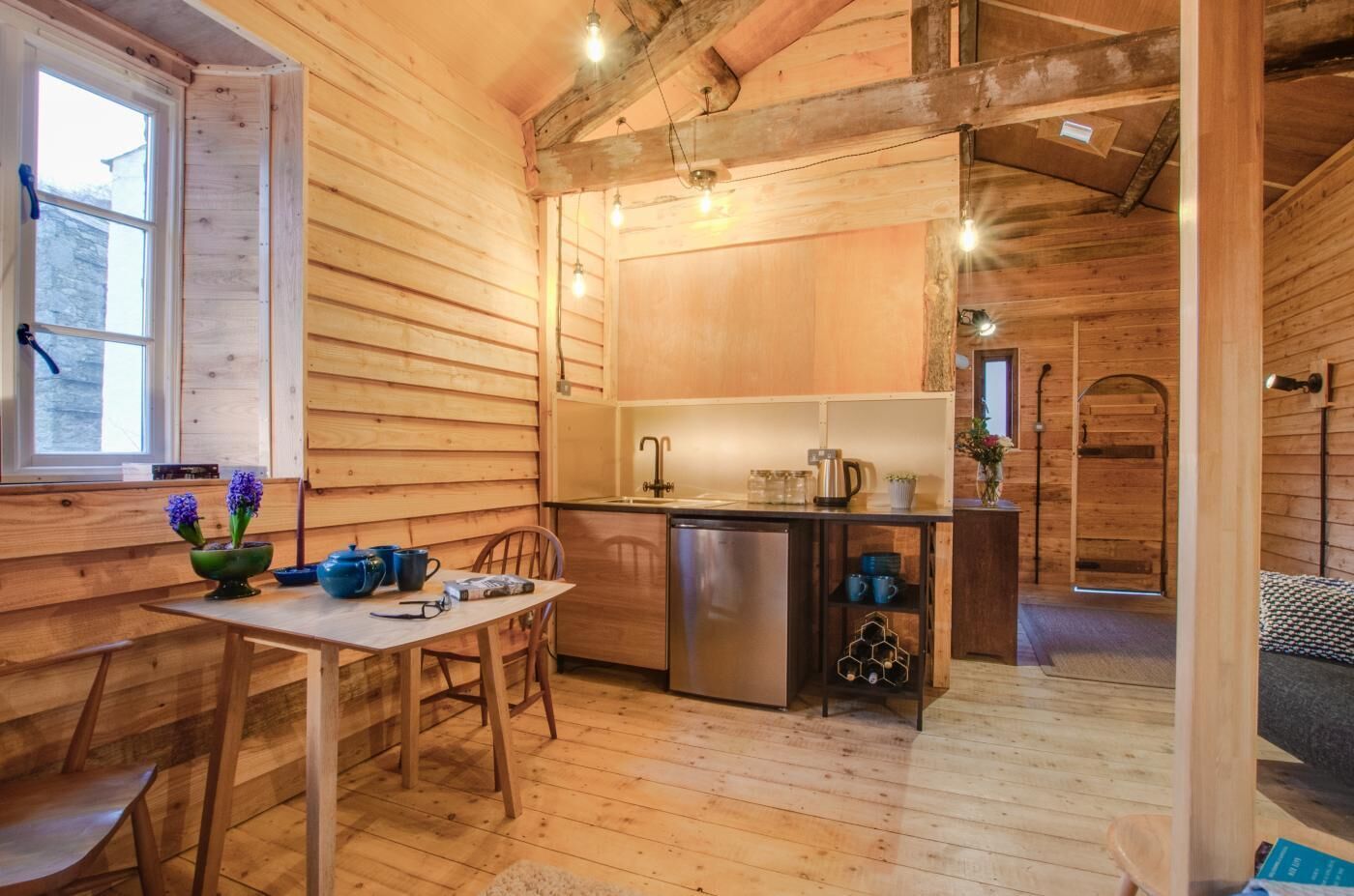 A cozy cabin interior with a wooden interior, a dining area with a table and chairs, a kitchen with a sink and stove, and a small bathroom with a shower.