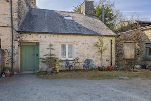 A stone building with a green door, a small window, and a table with chairs outside.