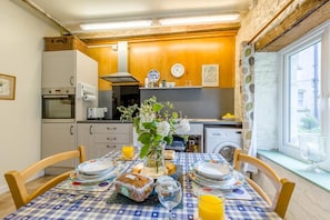 A compact kitchen with a dining table set for two, a washing machine, and a window with a view.