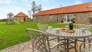 A patio with a table set for breakfast, a stone building with a red-tiled roof, and a children's play structure. - 3 Bed in nr Beadnell (oc-cr1279) (Beadnell)
