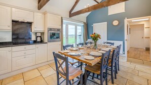 A kitchen with white cabinets, a black countertop, and a dining area with a wooden table set for four. - 3 Bed in nr Beadnell (oc-cr1279) (Beadnell)