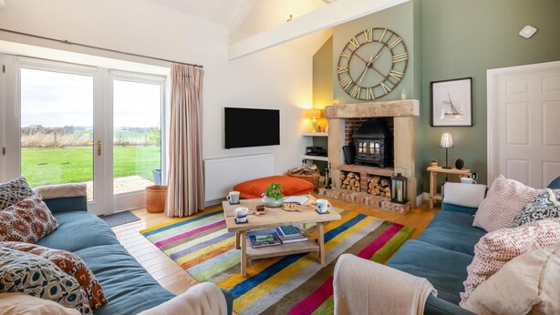 A cozy living room with a fireplace, a large clock, and a view of the outdoors. - 3 Bed in nr Beadnell (oc-cr1279) (Beadnell)