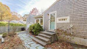 Une maison d’habitation avec un chemin de pierre menant à la porte d’entrée, entourée d’un feuillage automnal et d’une clôture en bois.