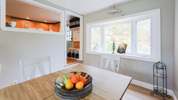 Un coin repas avec une table en bois, un saladier rempli de fruits et une fenêtre donnant sur l’extérieur.