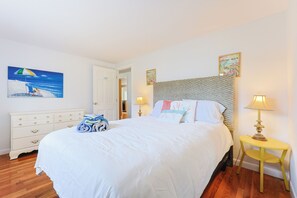 Une chambre à coucher bien rangée, avec un grand lit, une table de chevet avec une lampe, une commode et deux tableaux accrochés au mur.