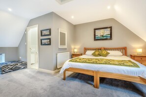 Un dormitorio con techo inclinado, una cama con colcha, lámparas de noche, un espejo y cuadros en la pared.