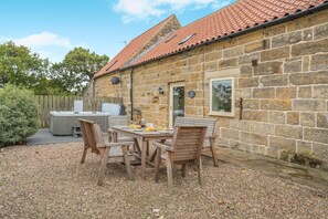 Un bâtiment en pierre avec un toit en tuiles, une terrasse avec une table et des chaises, et un jacuzzi.