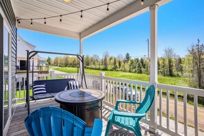 A covered outdoor deck with a grill, chairs, and a view of a green landscape. - Welcome to Slice of Haven with HOT TUB! (South Haven)