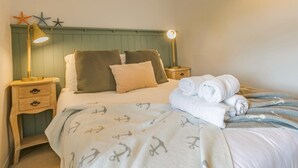 Een net opgemaakt bed met een geruit kussen, een bedlampje en opgerolde handdoeken aan de zijkant.