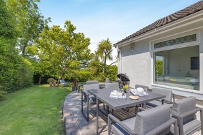 Un patio con una mesa dispuesta para el desayuno, rodeada de sillas y una ventana grande con vistas a un jardín.