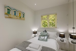 Un dormitorio con una cama, dos lámparas de noche, un cuadro, una ventana con persianas y un espejo.