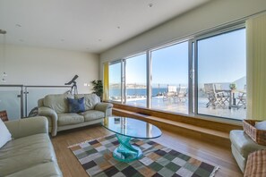 Un salon spacieux doté d’une grande fenêtre donnant sur un balcon aménagé avec du mobilier d’extérieur.