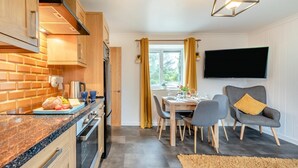 A modern kitchen with wooden cabinets, a granite countertop, and a dining area with a table and chairs. - 2 Bed in Tenby (oc-k26848) (Saint Florence)