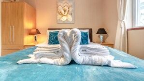 A hotel room with a bed, a fan, a painting, and a nightstand with a lamp. - 2 Bed in Tenby (oc-k26848) (Saint Florence)