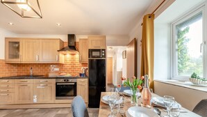A modern kitchen with wooden cabinets, a black refrigerator, and a dining area with a table set for four. - 2 Bed in Tenby (oc-k26848) (Saint Florence)