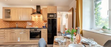A modern kitchen with wooden cabinets, a black refrigerator, and a dining area with a table set for four.
