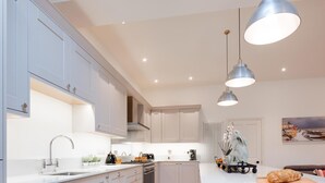 A modern kitchen with white cabinetry, a central island, pendant lighting, and a wooden floor. - 3 Bed in Cromer (oc-2241) (Cromer)