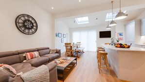 A modern living room with a brown sofa, a coffee table, and a dining area with wooden chairs and a white table. - 3 Bed in Cromer (oc-2241) (Cromer)