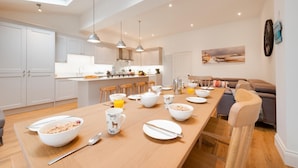 A modern kitchen with a central island, white cabinetry, pendant lighting, and a dining area with a wooden table set for breakfast. - 3 Bed in Cromer (oc-2241) (Cromer)