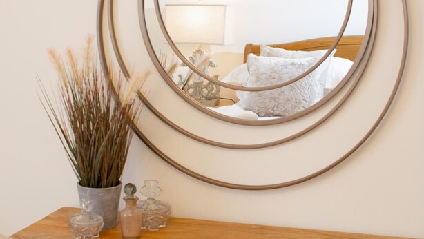 A wooden desk with a round mirror and a vase of dried plants. - 3 Bed in Cromer (oc-2241) (Cromer)