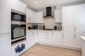 A modern kitchen with white cabinets, stainless steel appliances, and a wooden floor.
