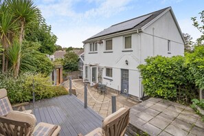 A two-story house with a patio area, outdoor seating, and a garden.