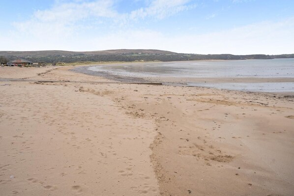 A sandy beach with footprints, a calm sea, and distant hills.
