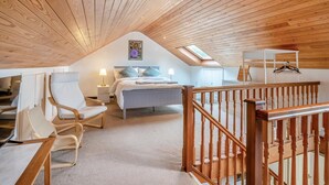 Ein Schlafzimmer mit schrägen Wänden, einem Bett, einem Sessel, einem Schreibtisch und einem Kleiderhaken.