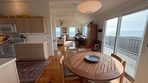 Eine moderne Küche mit Holzschränken, ein Essbereich mit einem runden Holztisch und Blick auf den Ozean durch große Fenster.