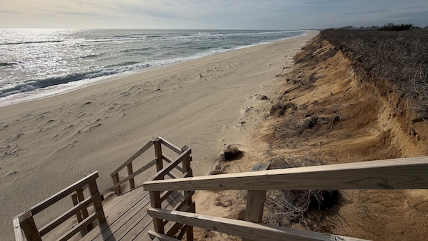 Ein hölzerner Steg führt zu einem Sandstrand mit Blick auf das Meer.