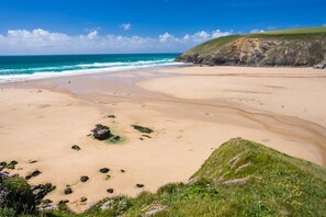 A coastal beach with a sandy shore, grassy areas, and a cliff. - 4 Bed in Mawgan Porth (oc-p00611) (Mawgan Porth)