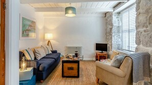 Un salon chaleureux avec un canapé bleu, un fauteuil beige, une table basse en bois et un mur en pierre.