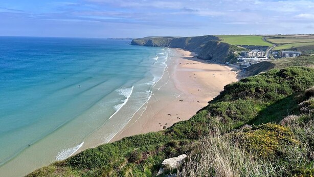 A coastal landscape with a sandy beach, cliffs, and a building complex. - 4 Bed in St. Mawgan (oc-p00610) (Saint Mawgan)