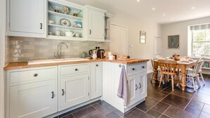A kitchen with white cabinets, a wooden countertop, and a dining area with a table and chairs. - 4 Bed in St. Mawgan (oc-p00610) (Saint Mawgan)