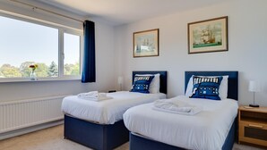 A hotel room with two beds, a large window with a view, and two framed pictures on the wall.