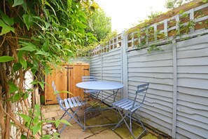 A patio with a table and chairs, a wooden shed, and a white fence. - 2 Bed in Cley (oc-1776) (Cley next the Sea)