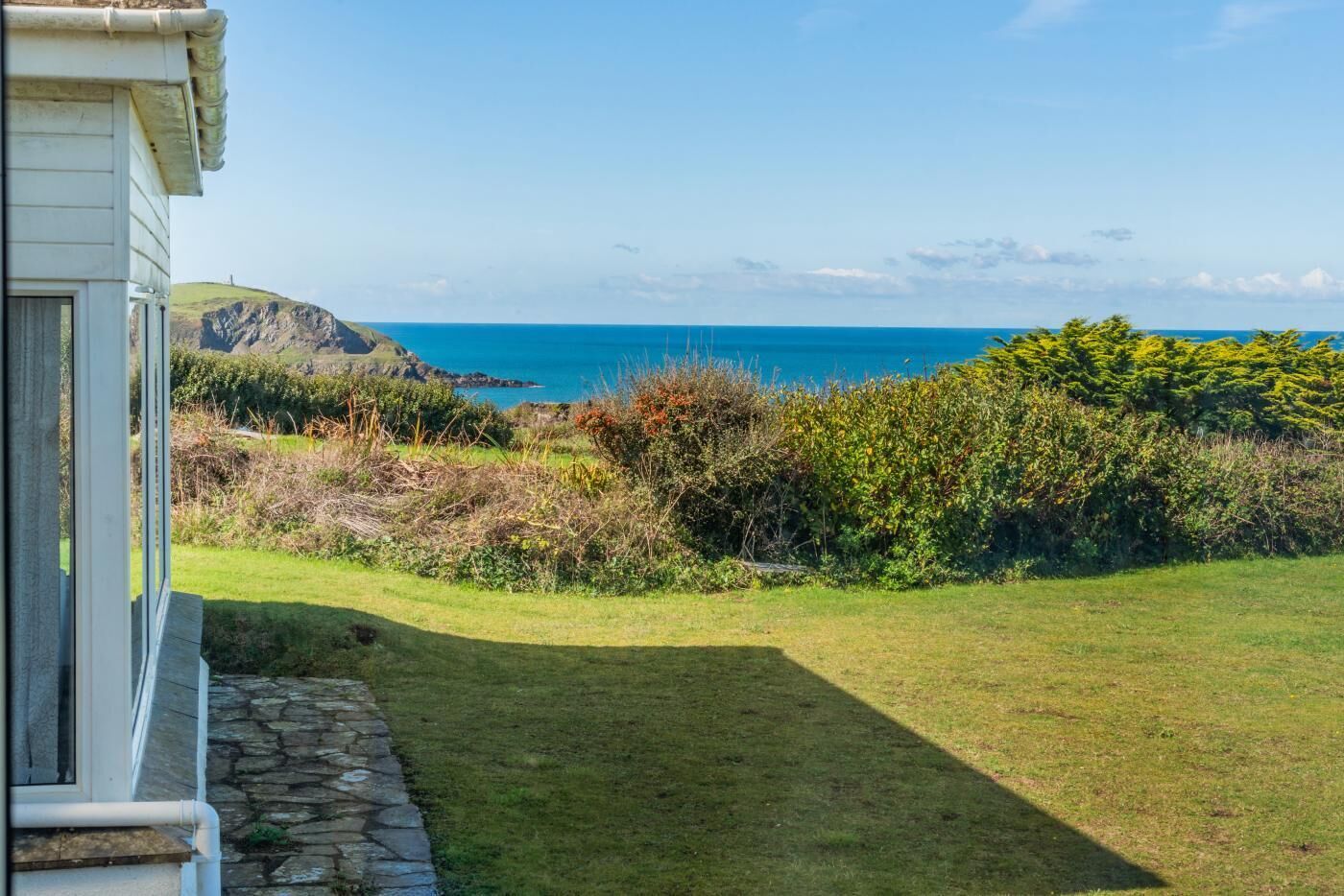 A house with a stone pathway leading to a grassy lawn and a view of the ocean.