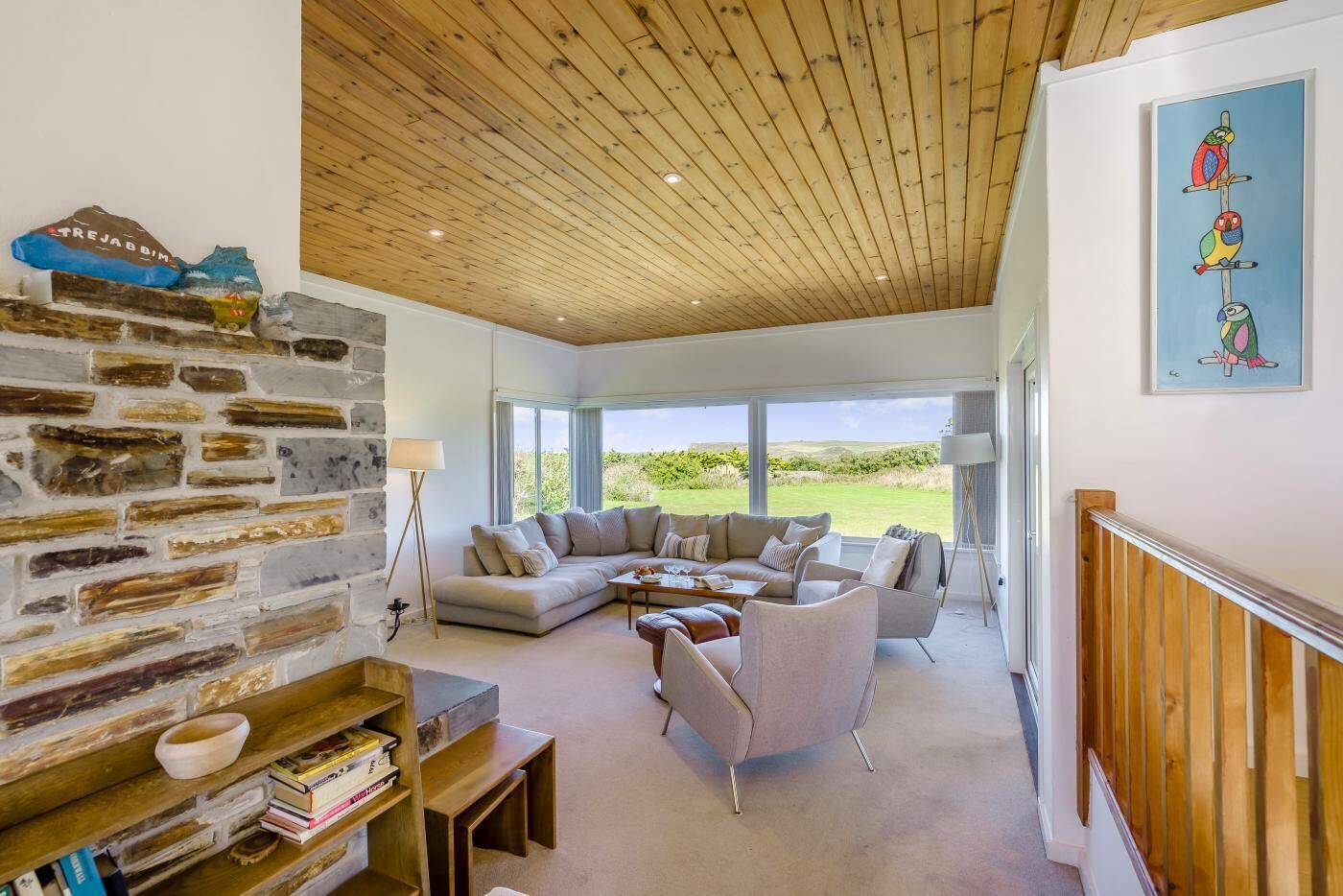Ein geräumiges Wohnzimmer mit Steinwand, Holzboden und einem großen Fenster mit Blick ins Freie.
