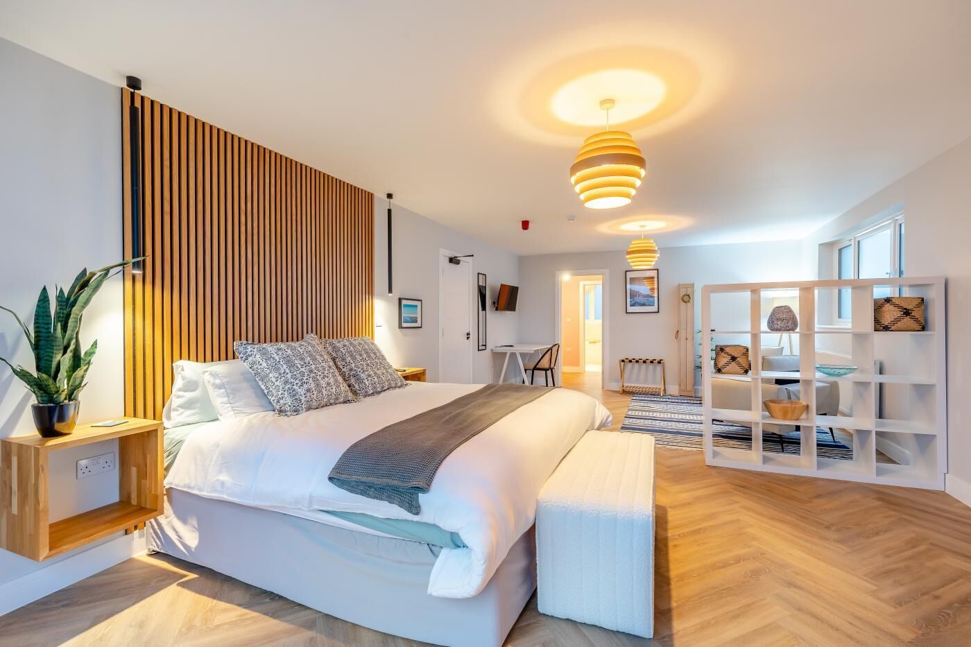 A modern bedroom with a large bed, wooden panel wall, and a white wardrobe.