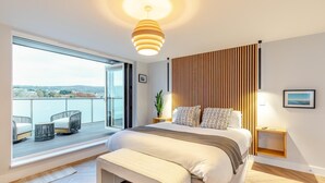 A modern bedroom with a large bed, a view of the outdoors, a balcony with seating, and a wooden slatted wall. - 10 Bed in Shanklin (oc-t33547) (Shanklin)