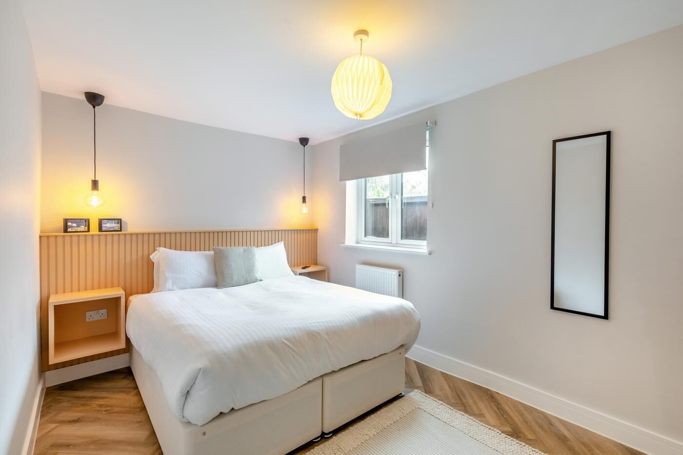 Une chambre moderne avec un grand lit, des tables de chevet, une fenêtre et un luminaire suspendu.