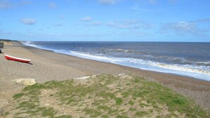A pebble beach with a red boat and a lifebuoy. - 2 Bed in Weybourne (oc-1789) (Weybourne)