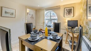 A dining area with a table set for two, a window with a view, and a television on a stand. - 2 Bed in Weybourne (oc-1789) (Weybourne)