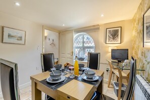 A dining area with a table set for two, a window with a view, and a television on a stand. - 2 Bed in Weybourne (oc-1789) (Weybourne)