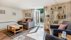 A living room with a sofa, a coffee table, a bookshelf, and a view through a glass door. - 2 Bed in Weybourne (oc-1789) (Weybourne)
