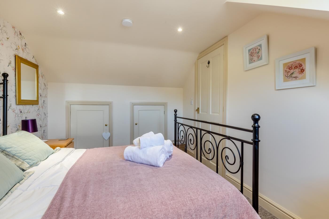 A bedroom with a bed, a nightstand, a lamp, a door, and framed pictures on the wall.