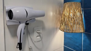 A white hair dryer mounted on a wall with a power outlet, next to a blue-tiled wall and a woven lamp. - Sea View • 3 King Beds • Premium Comfort in BC (Balneário Camboriú)