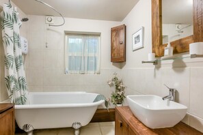A bathroom with a freestanding bathtub, a sink, a wooden cabinet, a window with curtains, and a mirror with a wooden frame. - 1 Bed in Stanhoe (oc-1792) (Stanhoe)